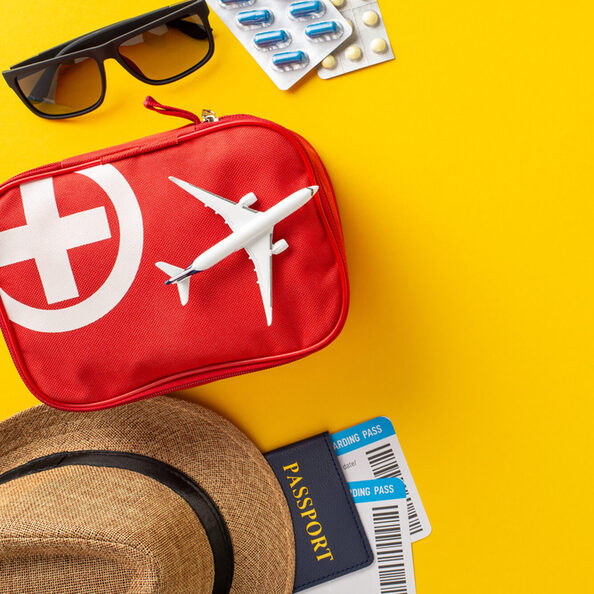 Travel safety essentials arranged with a red first aid kit, airplane, and passport against a vibrant yellow backdrop. Highlights health preparation for trips